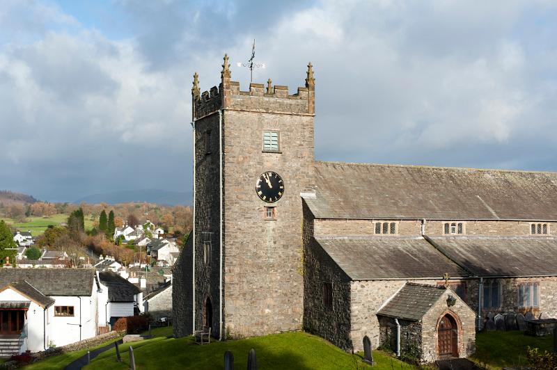 View of the old stone building and clock tower of St Michael and All Angels Church in the quaint whitewashed village of Hawkshead in the Lake District in Cumbria
